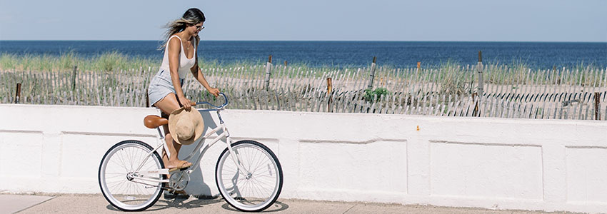 Girl riding Retrospec Chatham Beach Cruiser on bike path in front of ocean