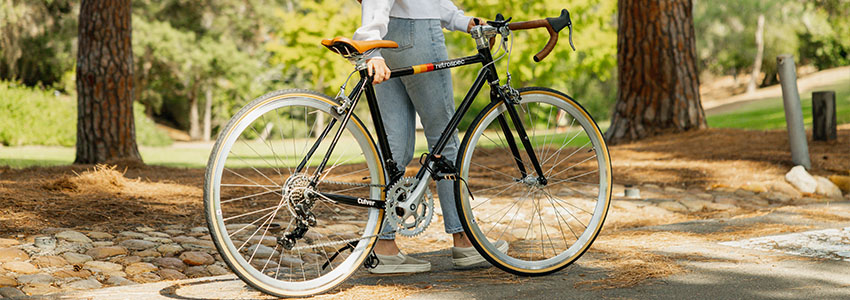 Girl standing behind black Retrospec Culver Road Bike in a park on a bike path