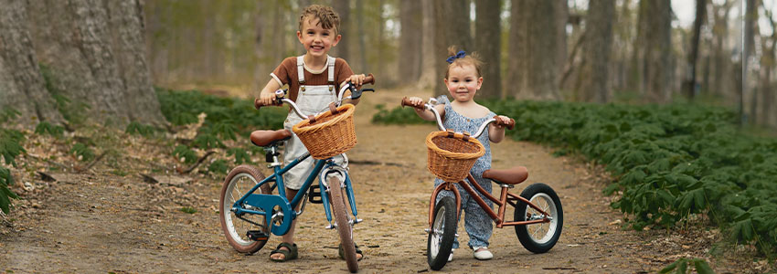 2 children standing behind 2 bikes on a forested path