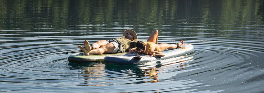 2 people laying on Retrospec Weekender Inflatable Paddle Boards on lake