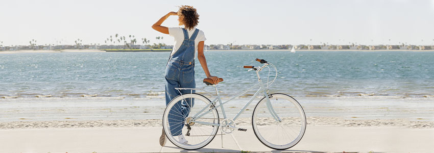 Girl standing behind Retrospec Kinney Mixte Bike on beach looking out towards water