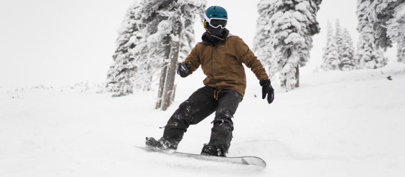 Person snowboarding down snowy mountain wearing snow jacket, helmet, and goggles