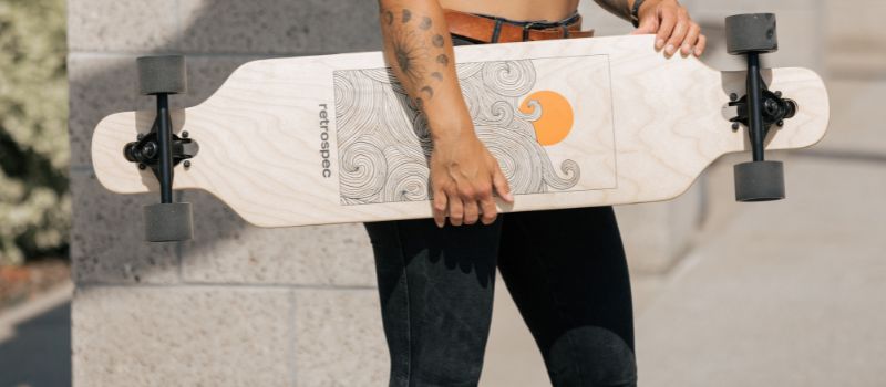 person holding longboard with a wooden deck designed with wave illustrations