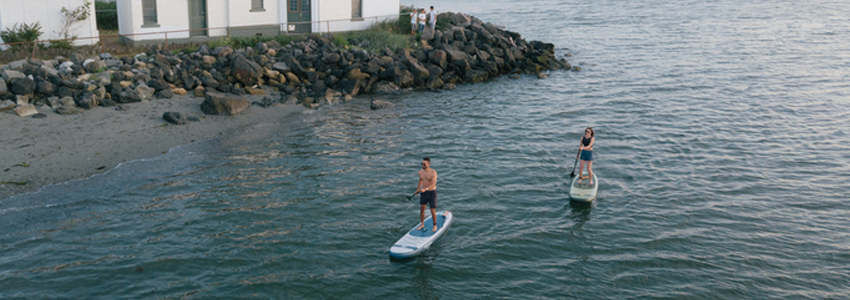 Two people paddleboarding around a lighthouse