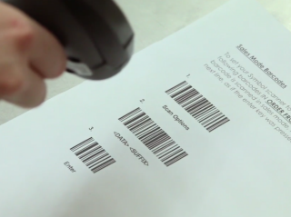 Photo d'une main tenant un lecteur pointé sur 3 codes-barres