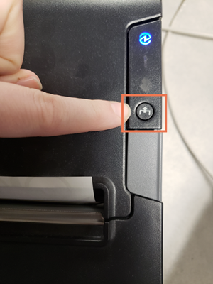Foto de la impresora con un dedo apuntando al botón Feed y el botón resaltado