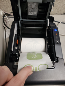 Foto di due dita che tengono la carta di una stampante per ricevute in una stampante aperta